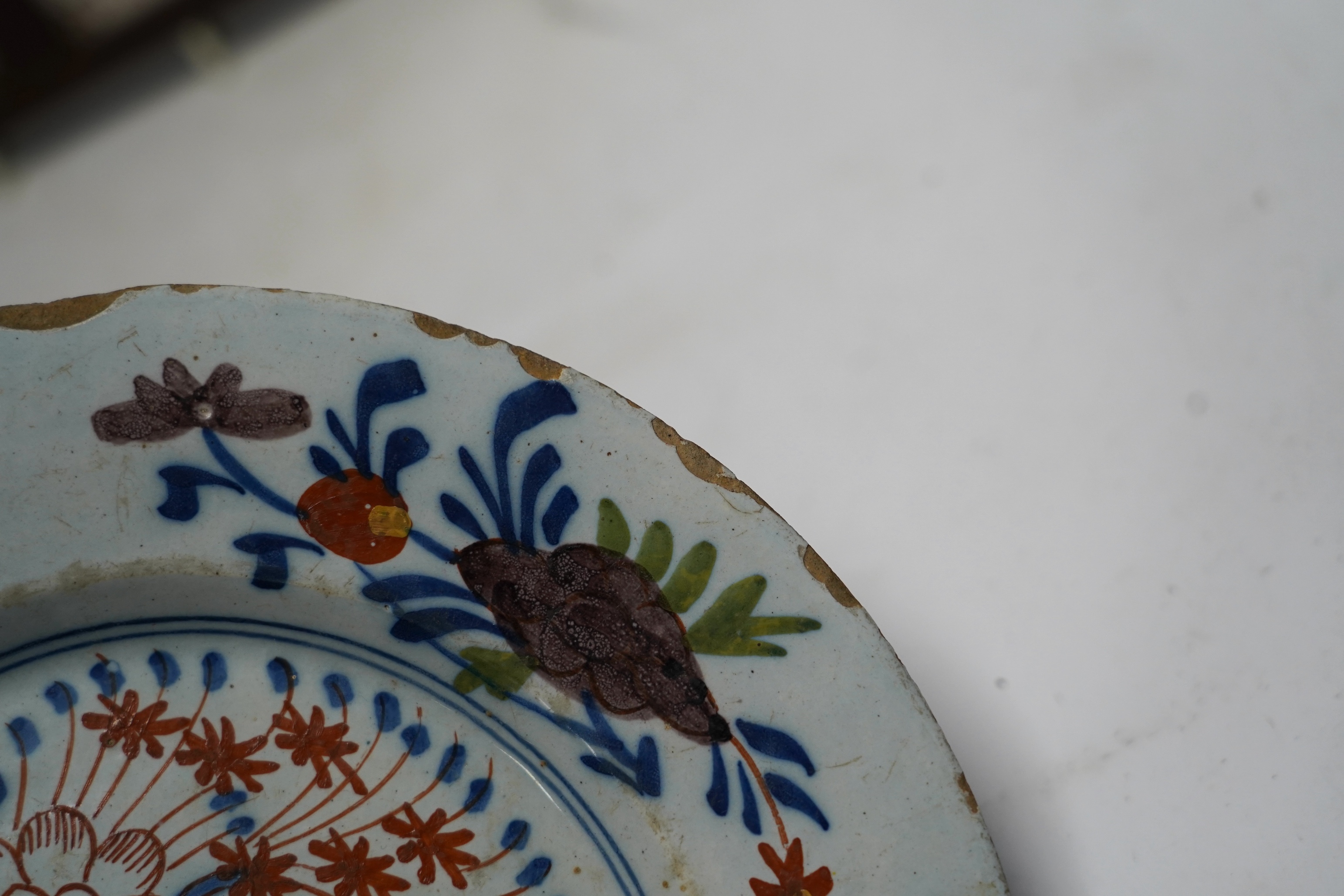 An 18th century Delft polychrome plate, 23cm diameter, and two framed tiles. Condition - tiles poor, plate with usual chipping to edges
